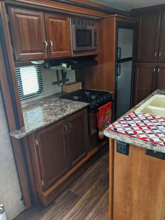 RV rental's compact kitchen boasts dark wood cabinets, built-in microwave, gas range, fridge, and light granite-look counters.. Other Other 2015