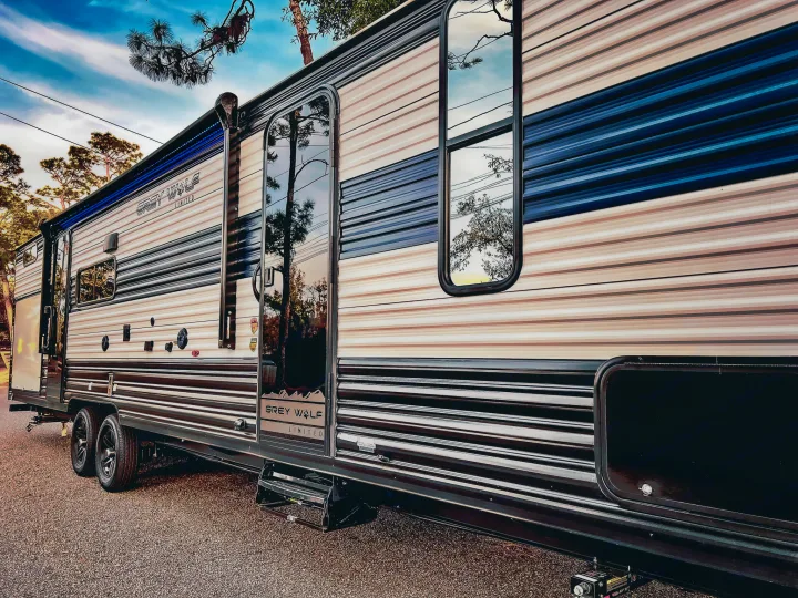 This stylish Grey Wolf Limited RV rental, parked on gravel, features blue LED awning lights and window reflections of trees and sky.. Forest River Cherokee Grey Wolf 2024