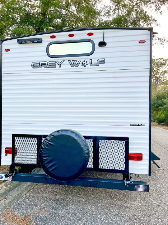 Rear view of a white Grey Wolf travel trailer rv rental. Features a spare tire, cargo rack, and Forest River logo.. Forest River Cherokee Grey Wolf 2024