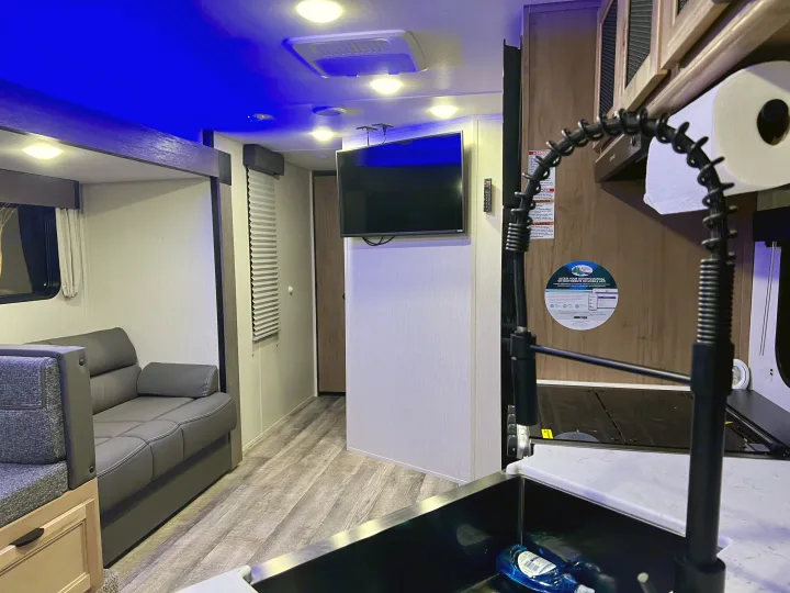 Explore this modern RV rental interior featuring a living area with a gray sofa, bunk area, TV, and kitchen with a flexible faucet.. Forest River Cherokee Grey Wolf 2024