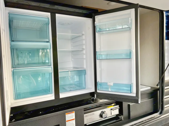 RV rental outdoor kitchen with an open mini-fridge, freezer drawers, Greystone grill, and a small sink for convenience.. Forest River Cherokee Grey Wolf 2024