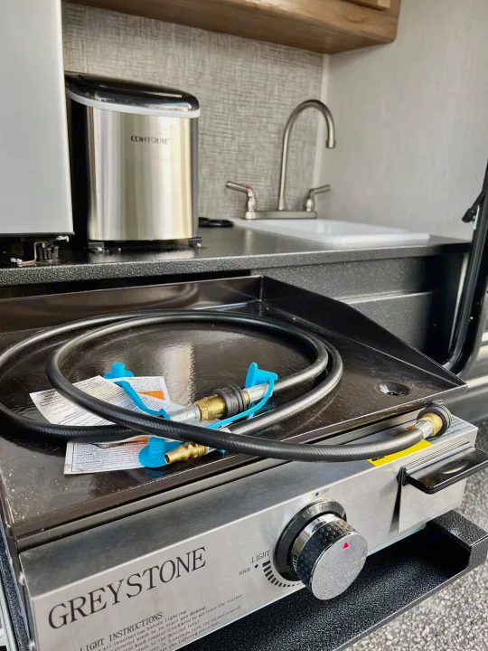 This RV rental's outdoor kitchen features a Greystone griddle, gas hose, Contoure appliance, and sink.. Forest River Cherokee Grey Wolf 2024