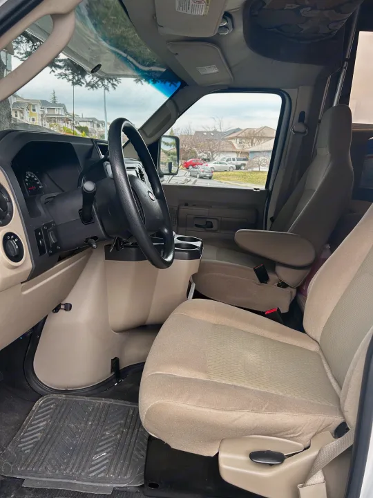 Interior of an RV rental van, showing the driver's cockpit, dashboard, and beige front seats with a view outside.. Adventurer Adventurer Motorhome 2012