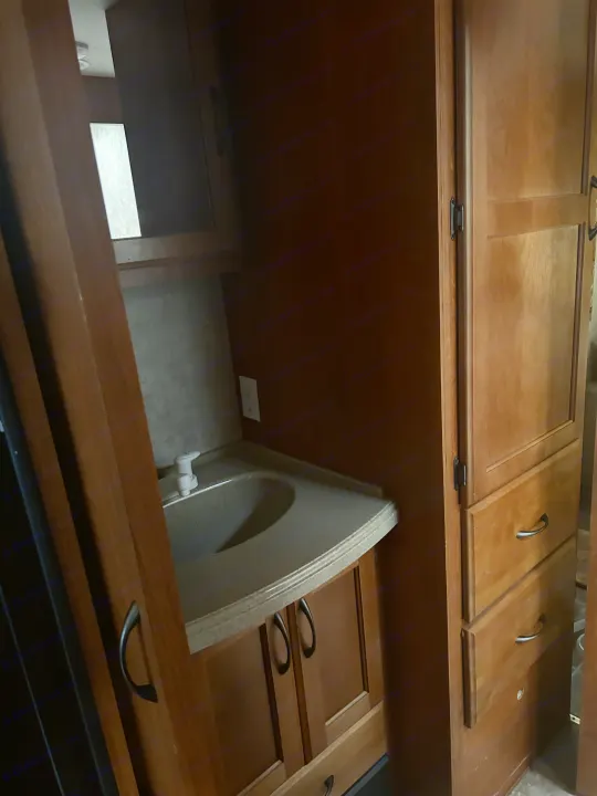Compact RV rental bathroom featuring a functional sink, light countertop, and wooden cabinets with storage drawers.. Adventurer Adventurer Motorhome 2012