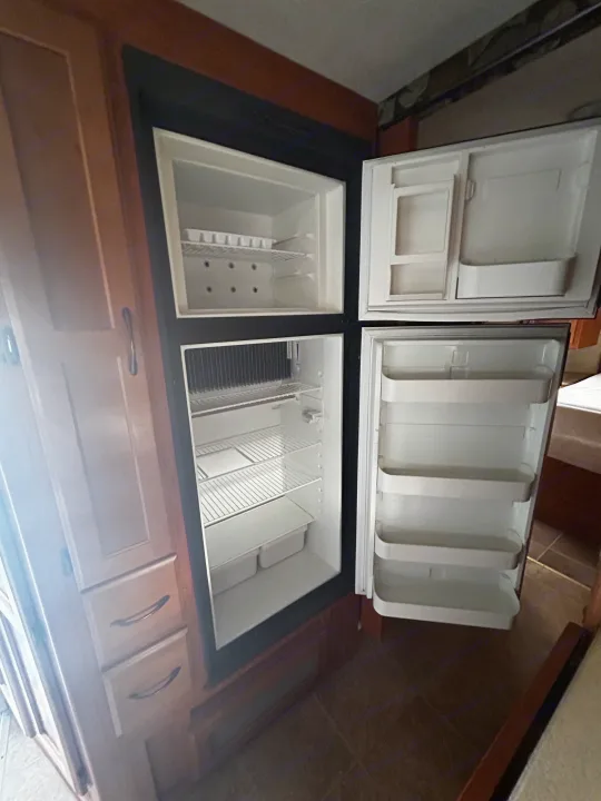 Inside a spacious RV rental refrigerator/freezer: sparkling clean, empty shelves and door bins, integrated into wood cabinets.. Adventurer Adventurer Motorhome 2012