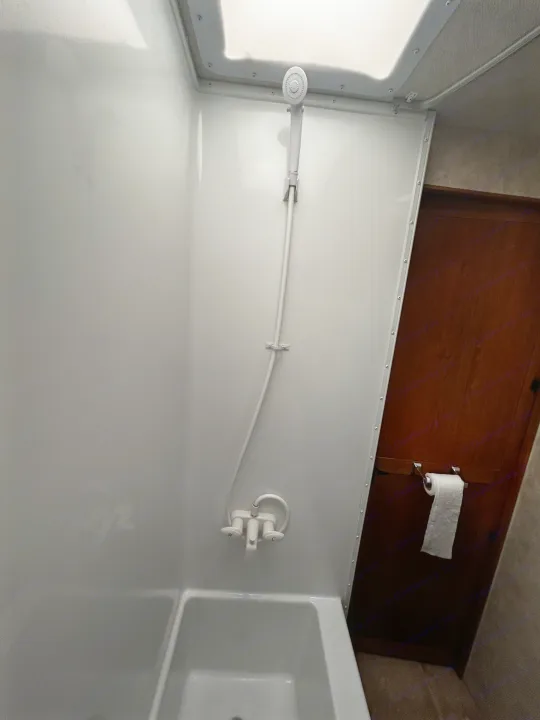 RV rental bathroom with white shower/tub, handheld showerhead, and toilet paper dispenser on a wooden door.. Adventurer Adventurer Motorhome 2012