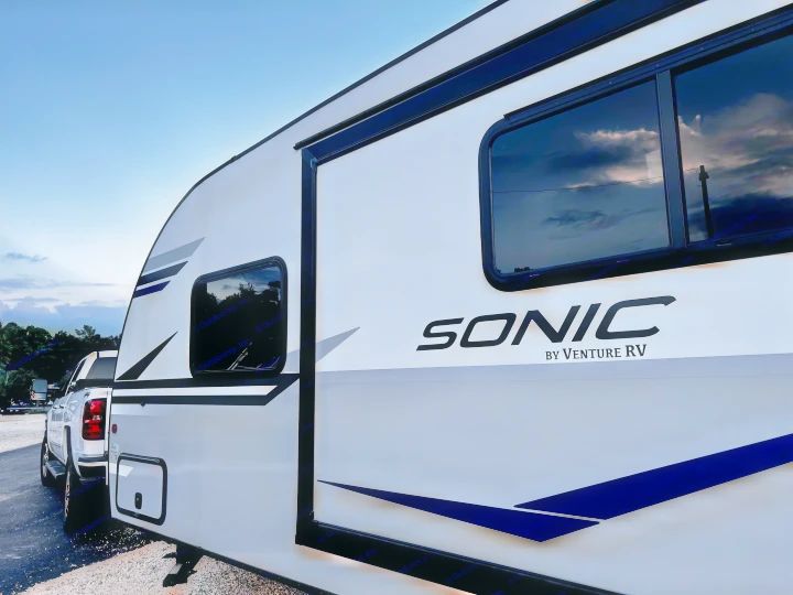 Modern white Sonic RV by Venture RV, hooked to a pickup truck, ready for an RV rental adventure under a cloudy sky.. Venture Rv Sonic 2022