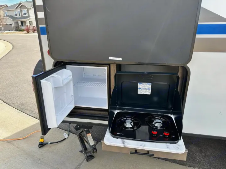 This RV rental features an outdoor kitchen with an open mini-fridge and a two-burner gas stove, perfect for meals on the go.. Venture Rv Sonic 2022