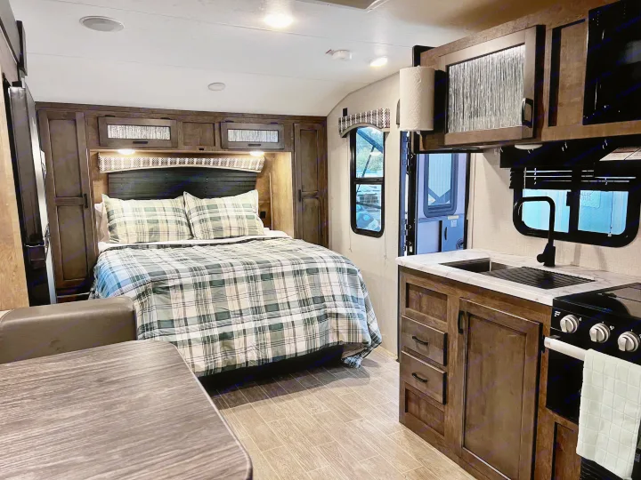 Experience comfort in this modern RV rental. Features a cozy bedroom with plaid bedding and a compact kitchen with sink and stove.. Venture Rv Sonic 2022