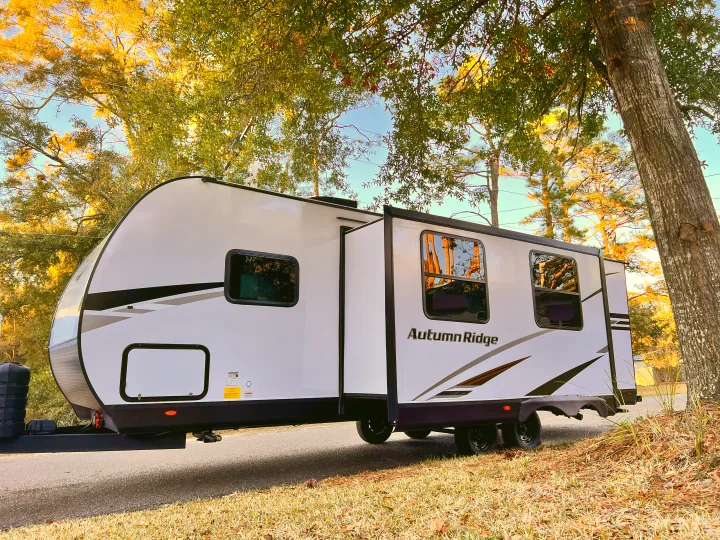White Autumn Ridge RV rental, featuring a slide-out and graphics, parked under golden-leaved trees for outdoor adventures.. Starcraft Autumn Ridge 2024