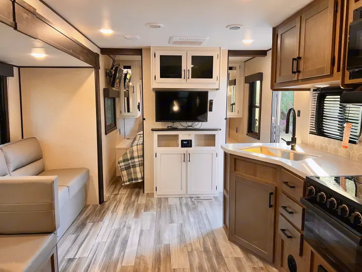 Modern RV rental showcasing a living space, kitchen with stove & sink, and an accessible bedroom, featuring wood-look flooring.. Starcraft Autumn Ridge 2024