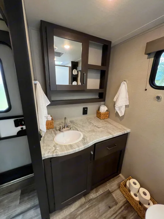 This RV rental features a modern, compact bathroom vanity with a sink, mirror, and ample storage for a comfortable stay.. Grand Design Transcend Xplor 2023
