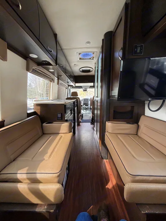 RV rental interior showcasing a comfortable, spacious living area with facing benches, wood floor, and storage.. Mercedes-Benz Sprinter RV Motorhome Campervan 2017