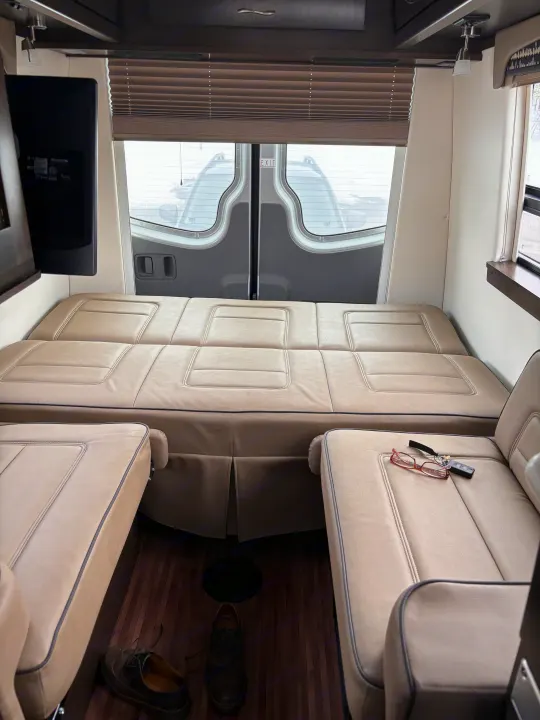 Interior of an RV rental: a light brown leather modular bed, two armchairs, a TV, and rear windows, perfect for trips.. Mercedes-Benz Sprinter RV Motorhome Campervan 2017