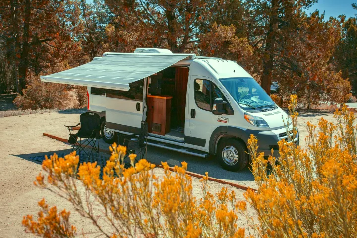 White RV rental with extended awning and camping chairs, ready for outdoor living, parked in an arid landscape.. Dodge Promaster 2500 2014