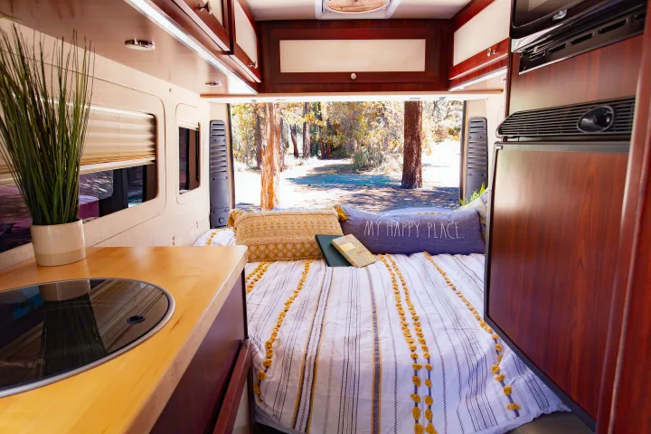 Serene RV rental interior with a cozy bed, "MY HAPPY PLACE" pillow, and a view of trees. Features a compact kitchen.. Dodge Promaster 2500 2014