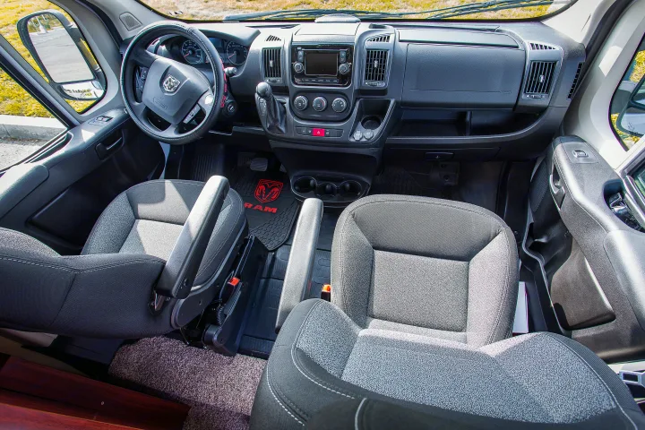 Spacious front cab of an RV rental van, showing the steering wheel, dashboard, seats, and infotainment system.. Dodge Promaster 2500 2014