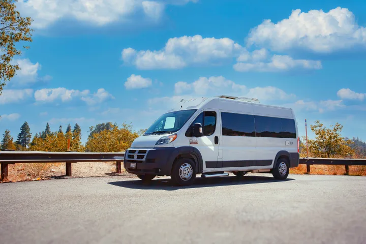 A white Ram ProMaster RV rental van is parked on a scenic road with a bright blue sky and clouds, perfect for travel adventures.. Dodge Promaster 2500 2014