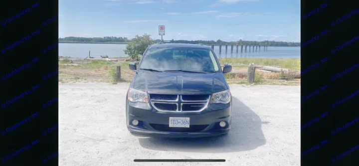 Front view of a black Dodge minivan (BC plate TD3 36N) parked by a scenic waterfront. Ideal for your RV rental trip.. Dodge Grand Caravan 2015