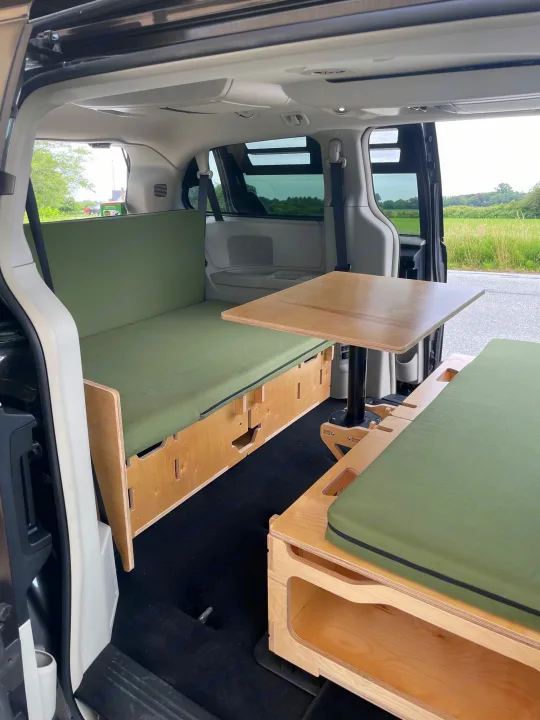 Minivan rv rental interior: clever modular wooden camper conversion with green cushioned benches and adjustable dining table.. Dodge Grand Caravan 2015