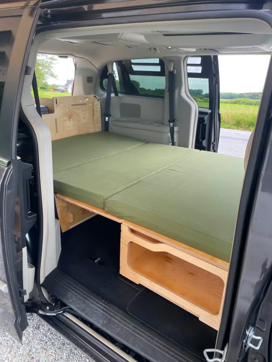 Converted minivan interior for rv rental: green mattress bed on wood platform with storage, ideal for vanlife.. Dodge Grand Caravan 2015