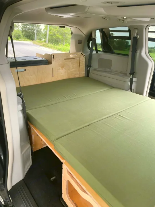 Inside this RV rental: a custom minivan camper with a green folding mattress & cooler, ready for adventure.. Dodge Grand Caravan 2015