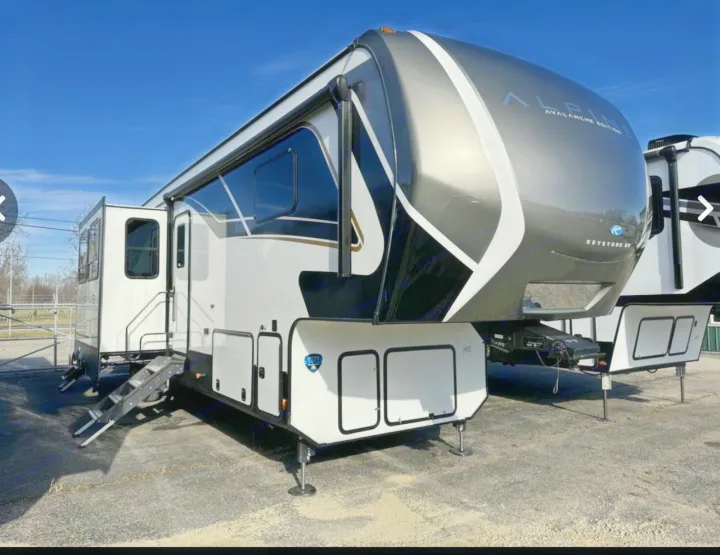 A modern, white and dark grey Keystone Alpine fifth-wheel RV rental with extended slides, parked outdoors.. Keystone Alpine Avalanche 2024