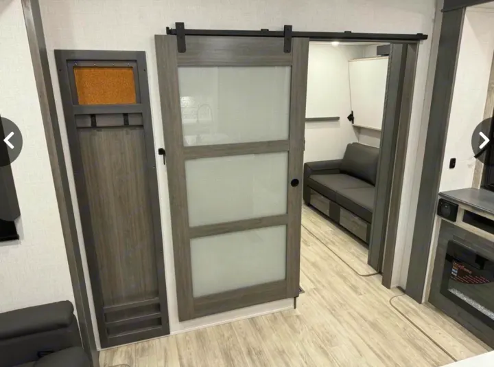 Modern RV rental interior with a sliding barn door, corkboard storage, and a lounge area visible through the doorway.. Keystone Alpine Avalanche 2024