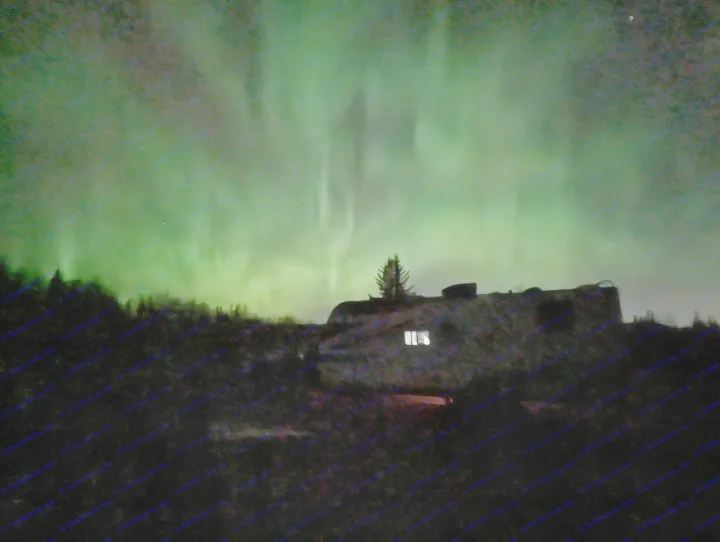 Vibrant green aurora borealis glows above an RV rental and dark trees, a spectacular night view.. Grand Design Imagine XLS 2023
