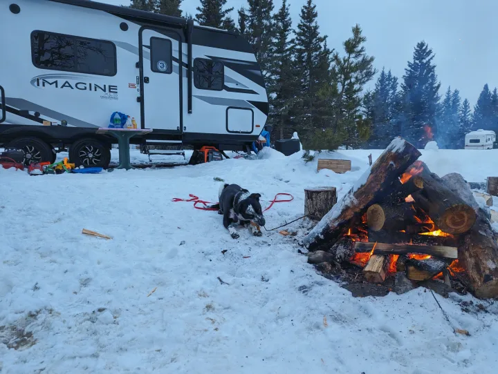 Enjoying winter camping: an Imagine XLS RV rental, warm campfire, and a dog playing in the snowy outdoors.. Grand Design Imagine XLS 2023
