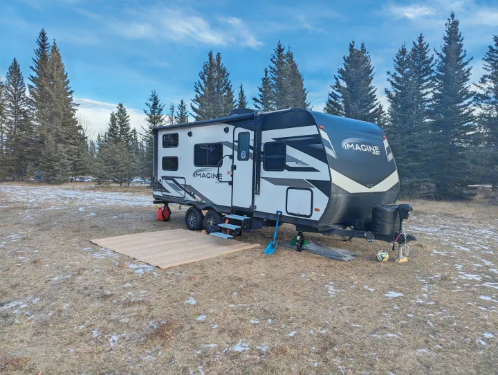 An RV rental, an Imagine XLS, parked in a snowy clearing amidst tall pines, ready for a winter adventure.. Grand Design Imagine XLS 2023