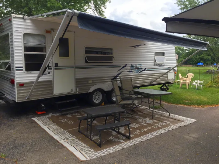 This RV rental boasts an extended awning & outdoor living area with tables, chairs & a mat for a comfortable campsite stay.. Keystone RV Springdale 2005