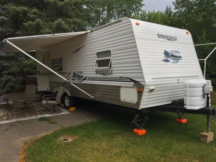 This white Springdale travel trailer, perfect for an RV rental, is parked with its awning extended over an outdoor seating area.. Keystone RV Springdale 2005