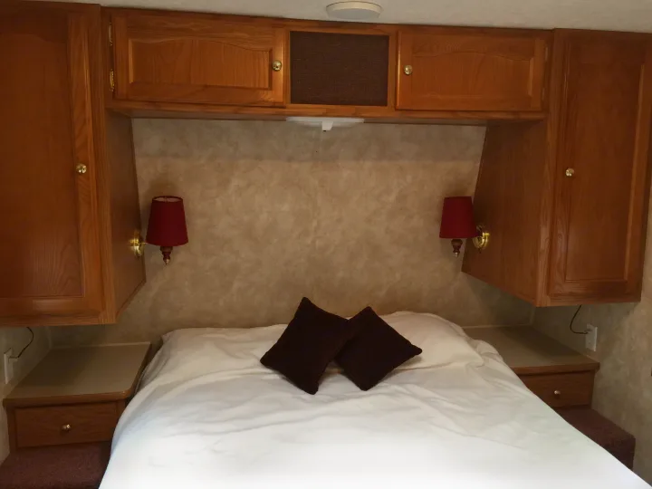 RV rental: A compact bedroom featuring a bed, built-in wooden cabinets overhead, wall lamps, and convenient nightstands.. Keystone RV Springdale 2005
