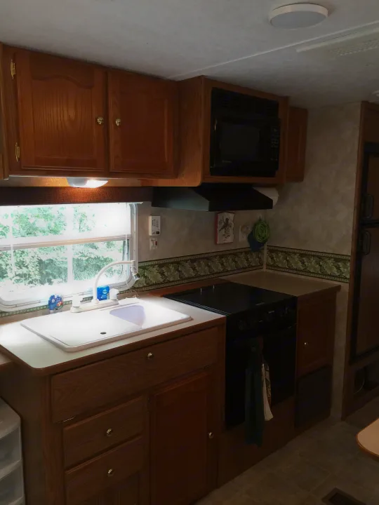 Well-equipped RV rental kitchen featuring a sink, stove, microwave, and overhead/under-counter storage.. Keystone RV Springdale 2005
