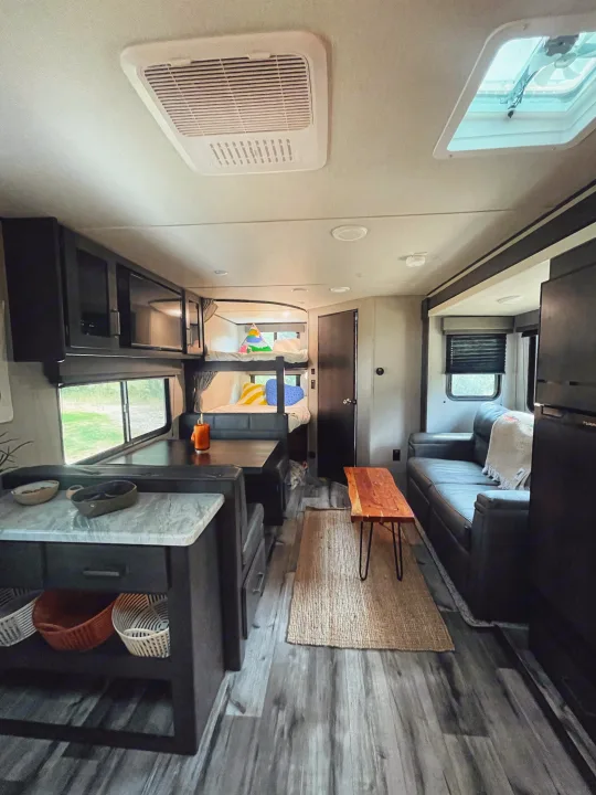 Spacious RV rental interior with kitchen, dining, bunk beds, and lounge area, featuring wood-look flooring and modern amenities.. Grand Design Transcend Xplor 2023
