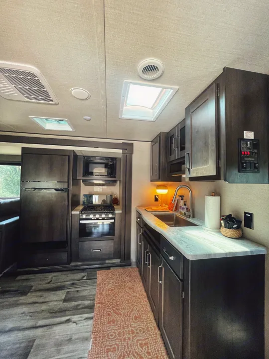 Modern RV rental kitchen with dark cabinets, sleek appliances, and a bright skylight. Perfect for your next adventure.. Grand Design Transcend Xplor 2023