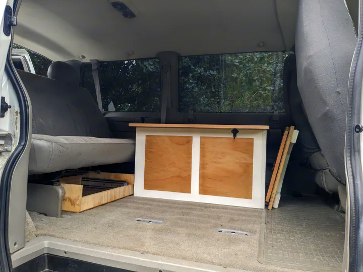 Inside a van, custom wood storage and a pull-out drawer sit by rear seats, ideal for an RV rental conversion.. Chevrolet Open Road 2002