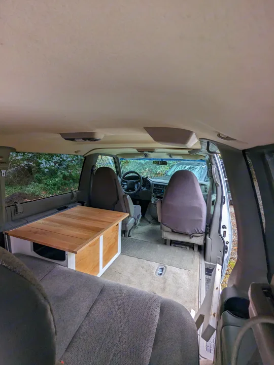 Inside an RV rental camper van: Features custom wooden sleeping platform, front seats, & dashboard.. Chevrolet Open Road 2002