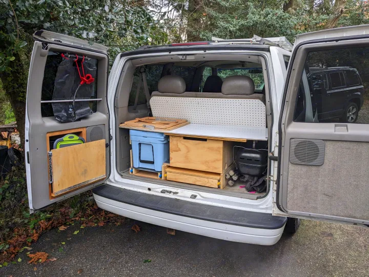 Inside an open RV rental van, a custom camper conversion features integrated kitchen, cooler, and storage solutions.. Chevrolet Open Road 2002