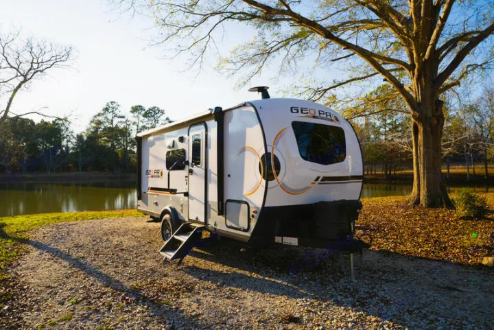 Geo Pro rv rental: a white travel trailer parked on gravel by a tranquil lake at sunset. Your waterfront camping adventure awaits!. Forest River Rockwood Geo Pro 2024