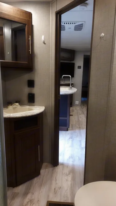 Inside an RV rental: a compact bathroom with sink and mirror, leading to a bright kitchen/living area.. Crossroads RV Zinger 2018