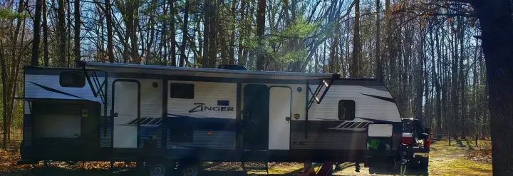 Large Zinger RV rental parked in a wooded campground with awning extended and outdoor kitchen open, ready for camping fun.. Crossroads RV Zinger 2018