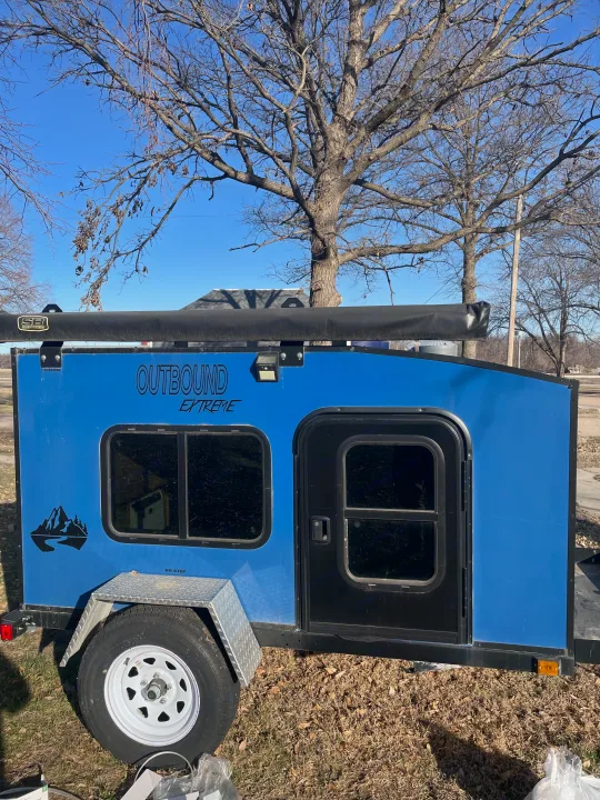 Blue "Outbound Extreme" teardrop trailer for RV rental, featuring an awning, window, and door.. County Outbound Extreme 2021