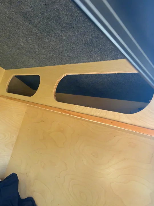 RV rental interior: Light wooden panels with two oval storage openings, and a dark gray carpeted upper section. Practical RV storage.. County Outbound Extreme 2021