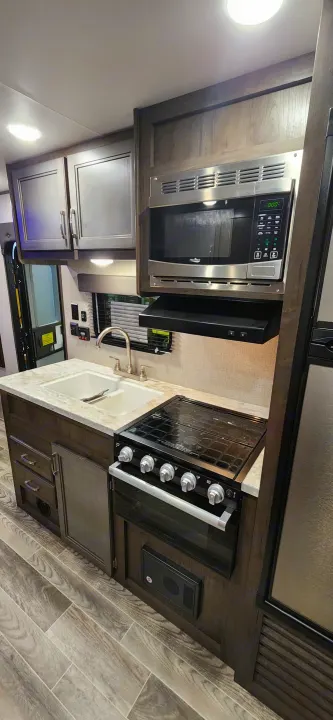Modern rv rental kitchen featuring a sleek microwave, gas range, and sink, set within compact cabinetry.. Jayco Jay Flight SLX 2021