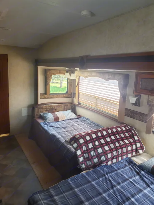 Inside an RV rental: a cozy bedroom with two beds, plaid blankets, and window blinds.. Keystone RV Springdale 2013