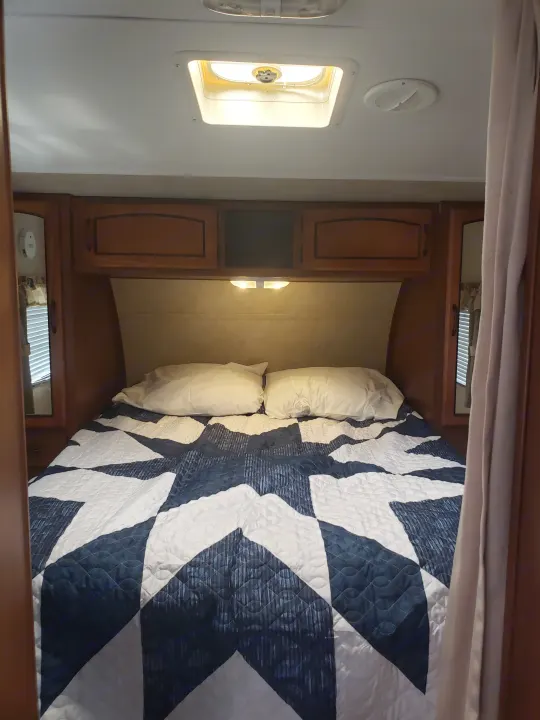 Experience comfort in this RV rental bedroom: blue/white quilted bed, wood cabinetry, and ceiling vents for a cozy trip.. Keystone RV Springdale 2013