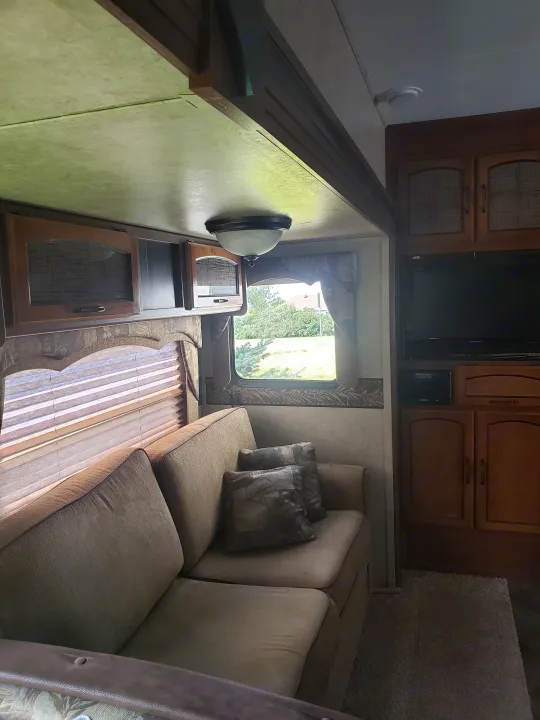 Cozy RV rental interior with a comfortable couch, window view, TV, and overhead storage cabinets.. Keystone RV Springdale 2013