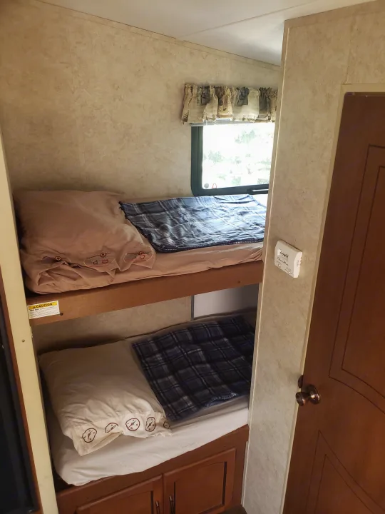 Cozy RV rental interior showing two bunk beds with bedding. Features include a window, thermostat, and built-in storage.. Keystone RV Springdale 2013